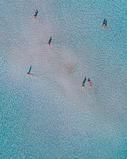 Drone footage of shallow blue waters and people swimming in it.