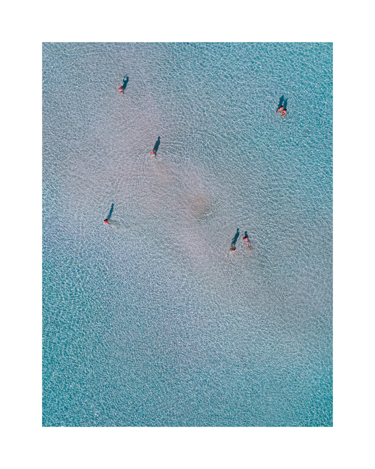 Drone footage of shallow blue waters and people swimming in it.