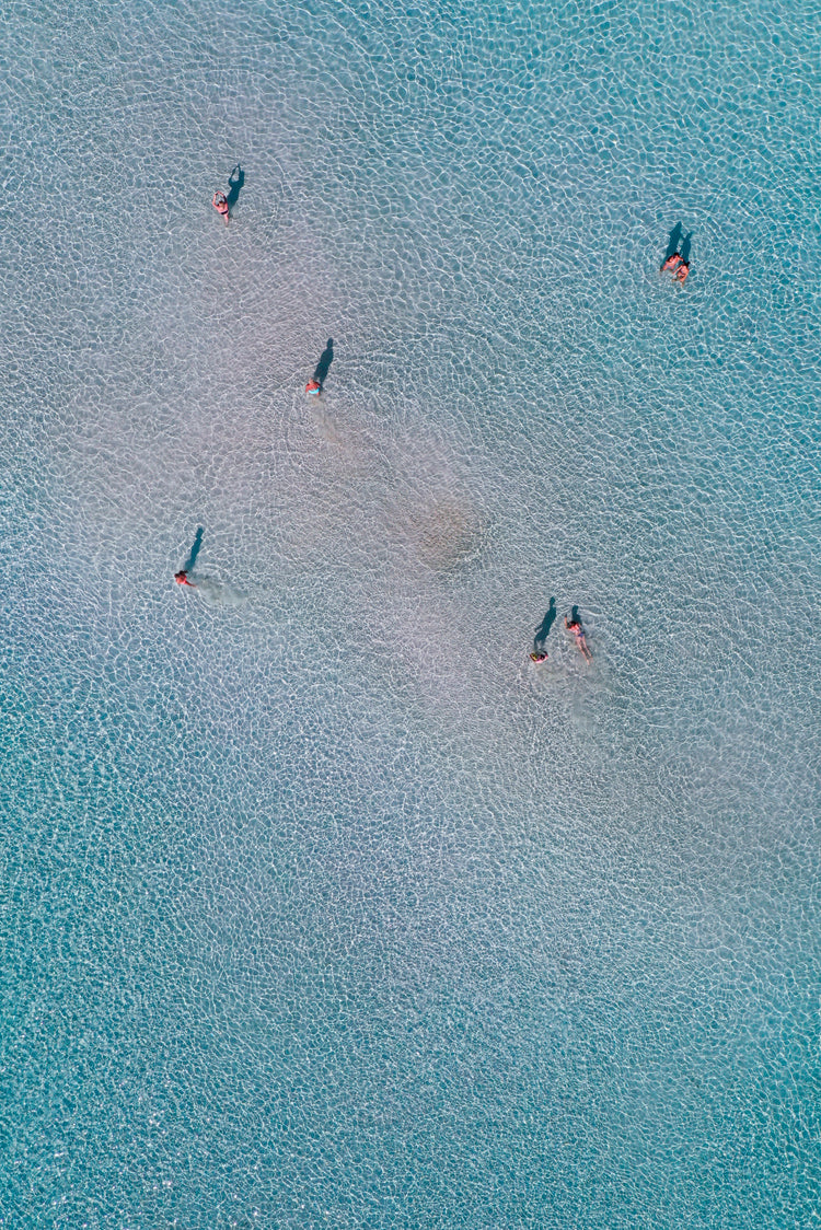 Drone footage of shallow blue waters and people swimming in it.