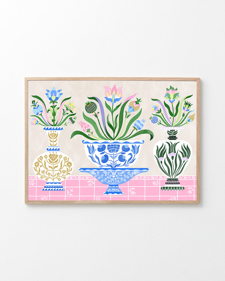 The Ceramics Poster, inspired by Swedish kurbits art, features a blue intricately designed central vase flanked by two smaller white and gold vases, all brimming with vibrant flowers and foliage on a pink patterned surface.