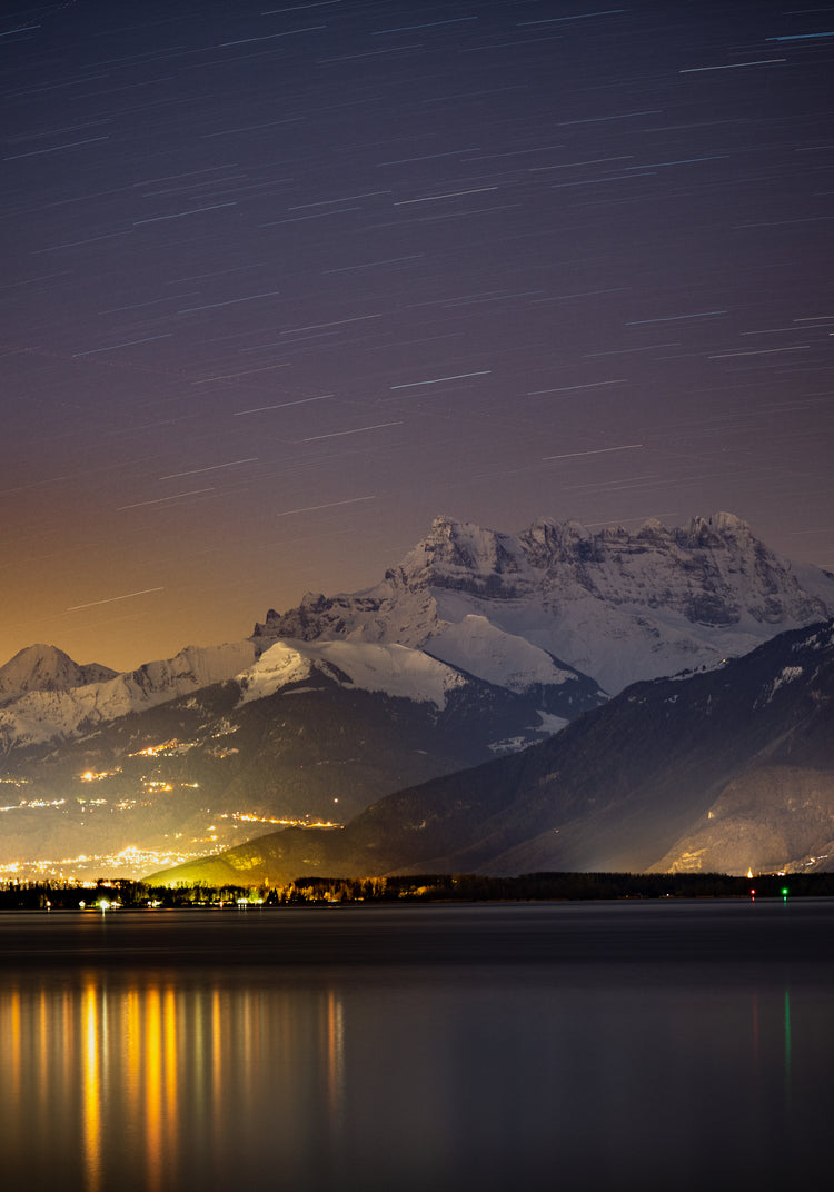 Star strewn sky above a city located next to a lake in the mountains.
