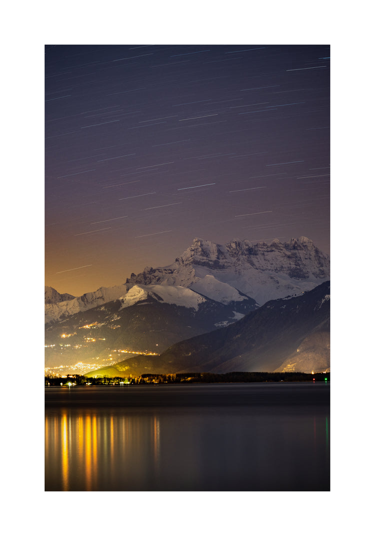 Star strewn sky above a city located next to a lake in the mountains.