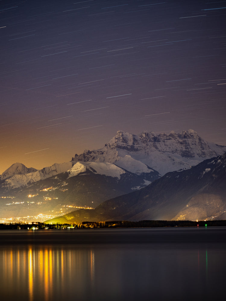Star strewn sky above a city located next to a lake in the mountains.