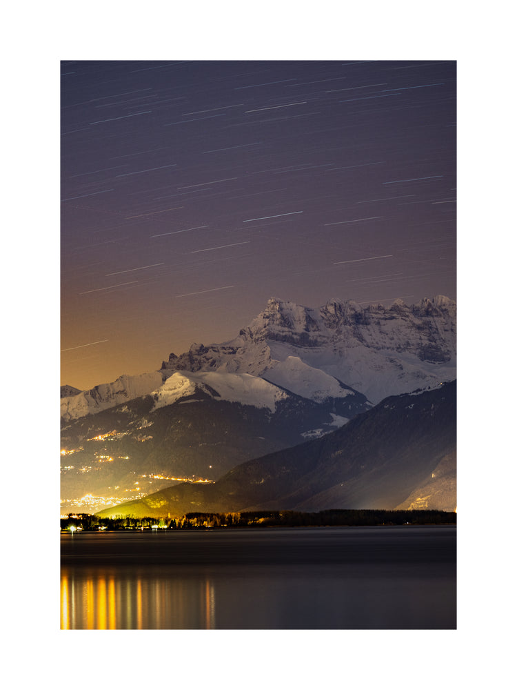 Star strewn sky above a city located next to a lake in the mountains.