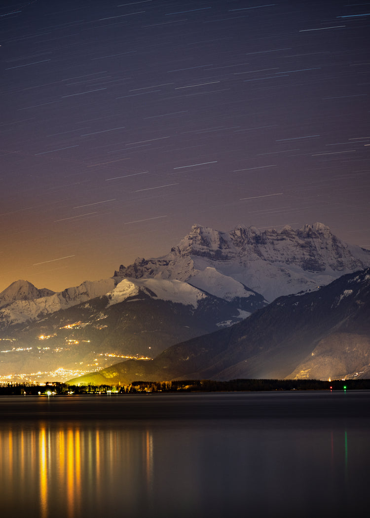 Star strewn sky above a city located next to a lake in the mountains.