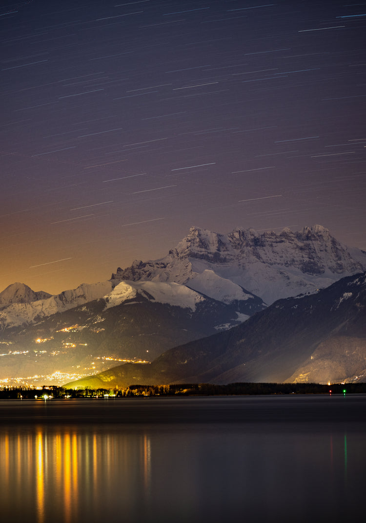 Star strewn sky above a city located next to a lake in the mountains.