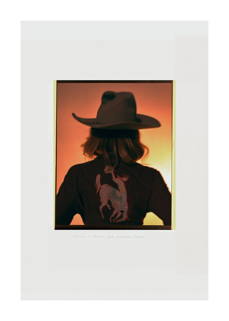 A woman with short hair and a cowboy hat dressed in a jacket with a cowboy print.