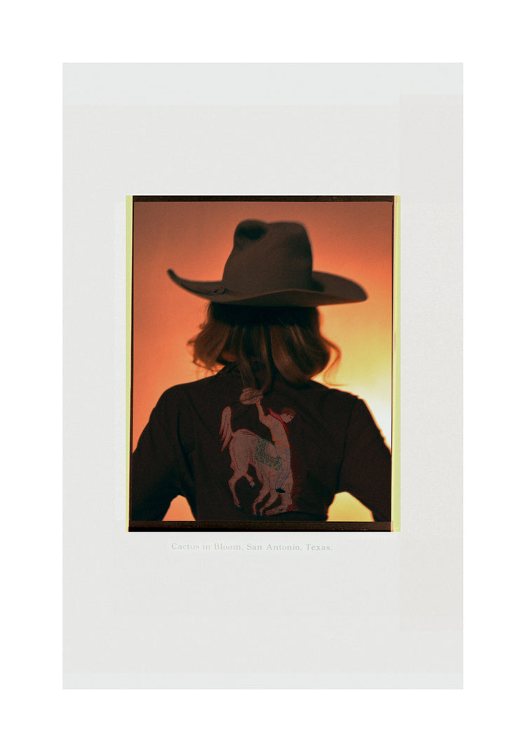 A woman with short hair and a cowboy hat dressed in a jacket with a cowboy print.