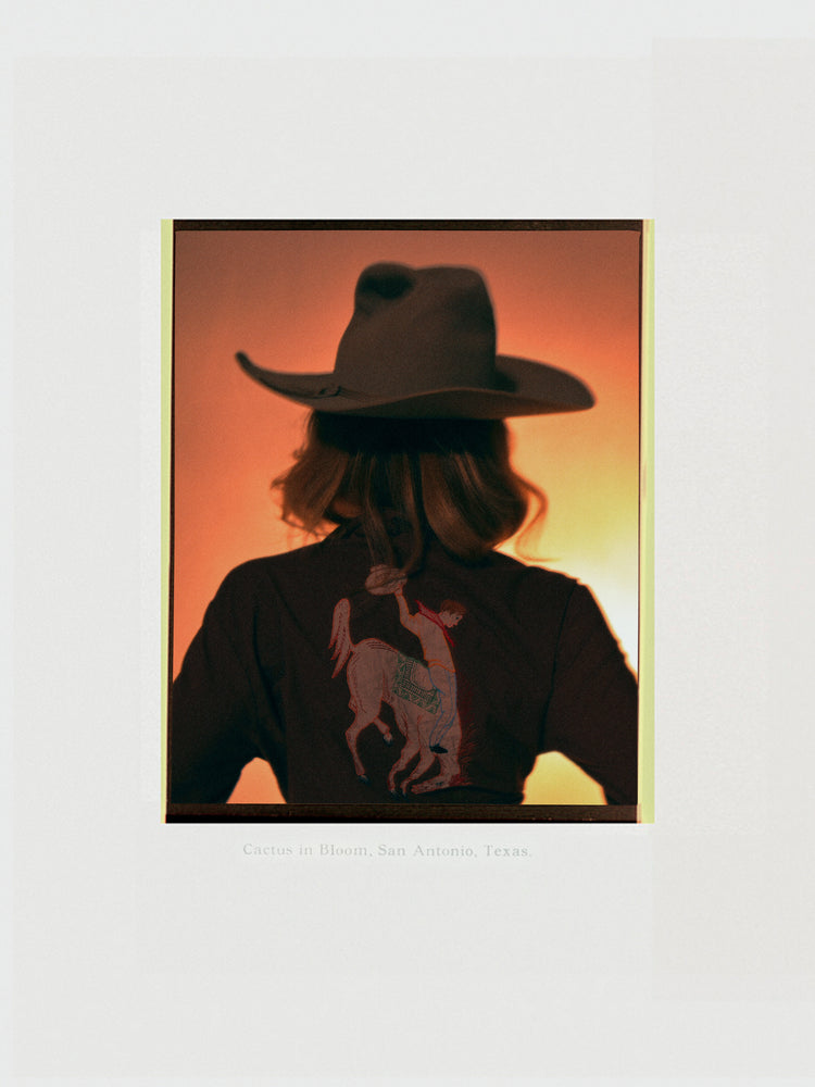A woman with short hair and a cowboy hat dressed in a jacket with a cowboy print.