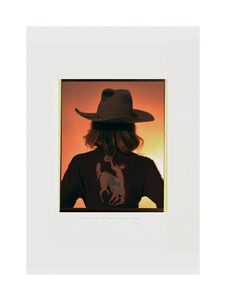 A woman with short hair and a cowboy hat dressed in a jacket with a cowboy print.