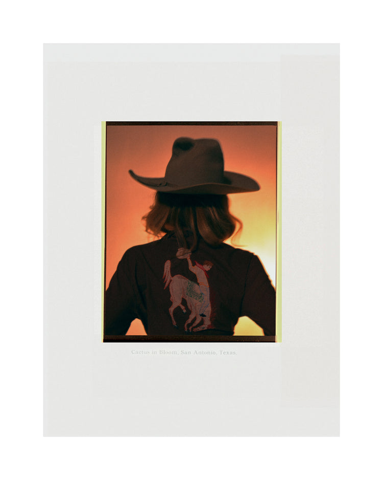 A woman with short hair and a cowboy hat dressed in a jacket with a cowboy print.