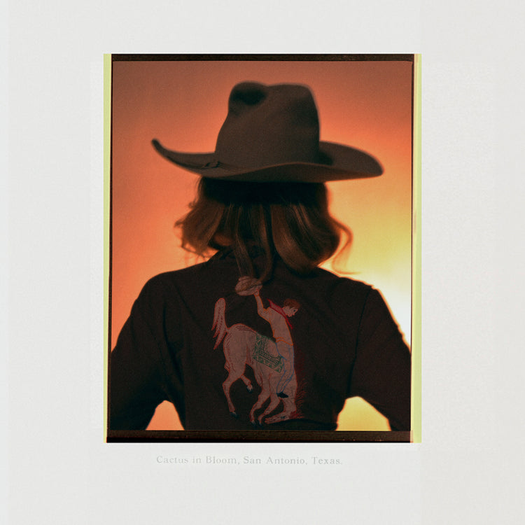 A woman with short hair and a cowboy hat dressed in a jacket with a cowboy print.