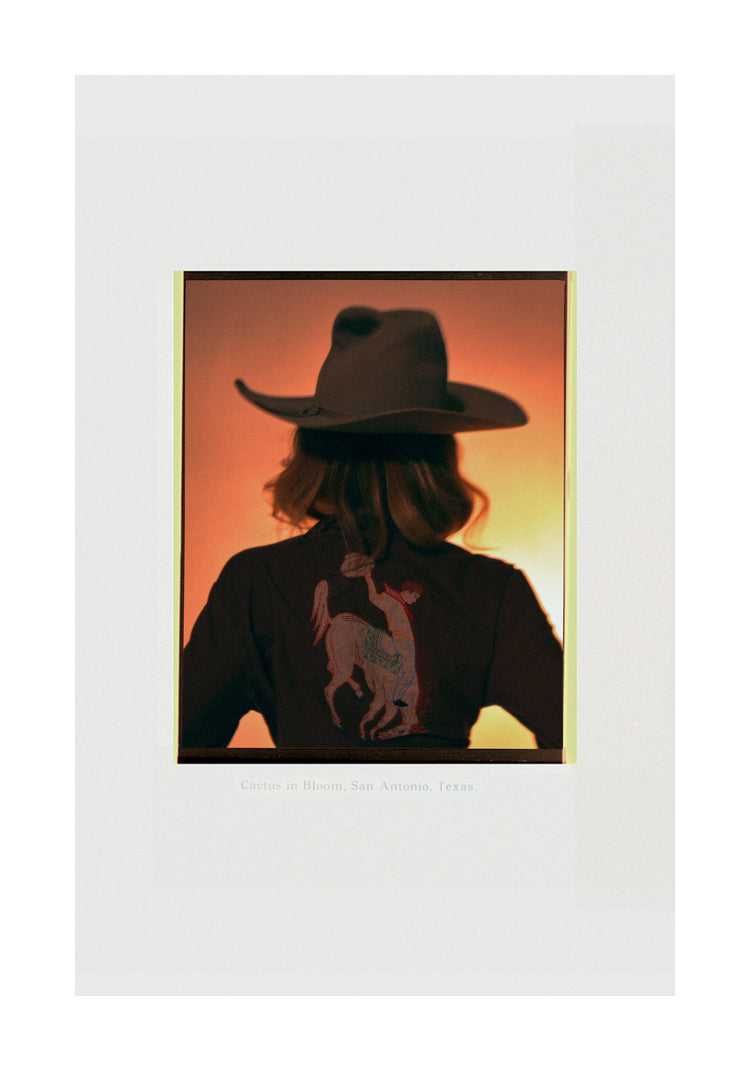 A woman with short hair and a cowboy hat dressed in a jacket with a cowboy print.