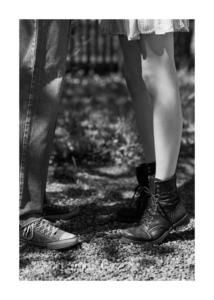 The feet of a woman standing on tiptoe kissing a man in converse sneakers.