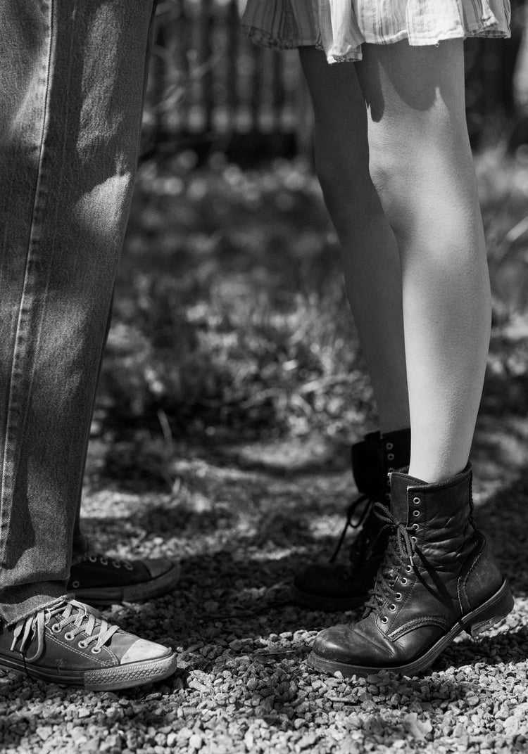 The feet of a woman standing on tiptoe kissing a man in converse sneakers.