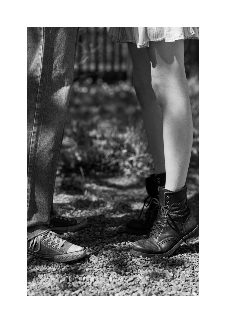 The feet of a woman standing on tiptoe kissing a man in converse sneakers.