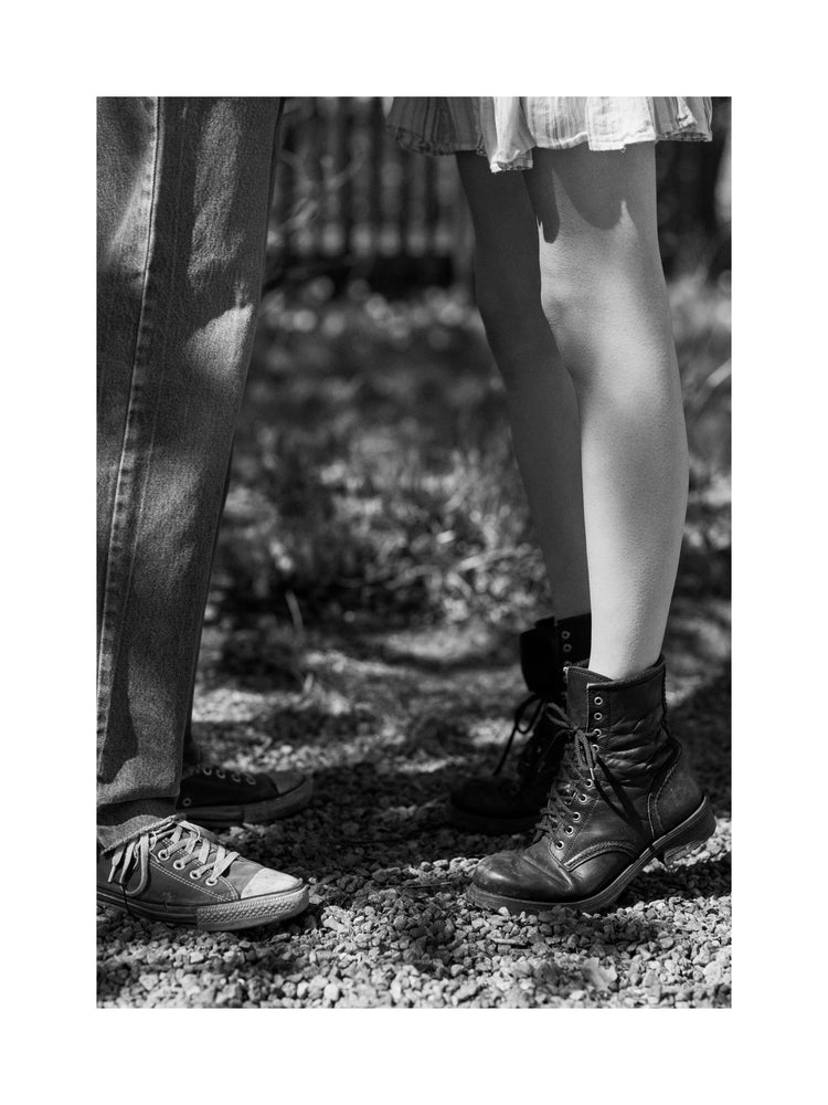 The feet of a woman standing on tiptoe kissing a man in converse sneakers.