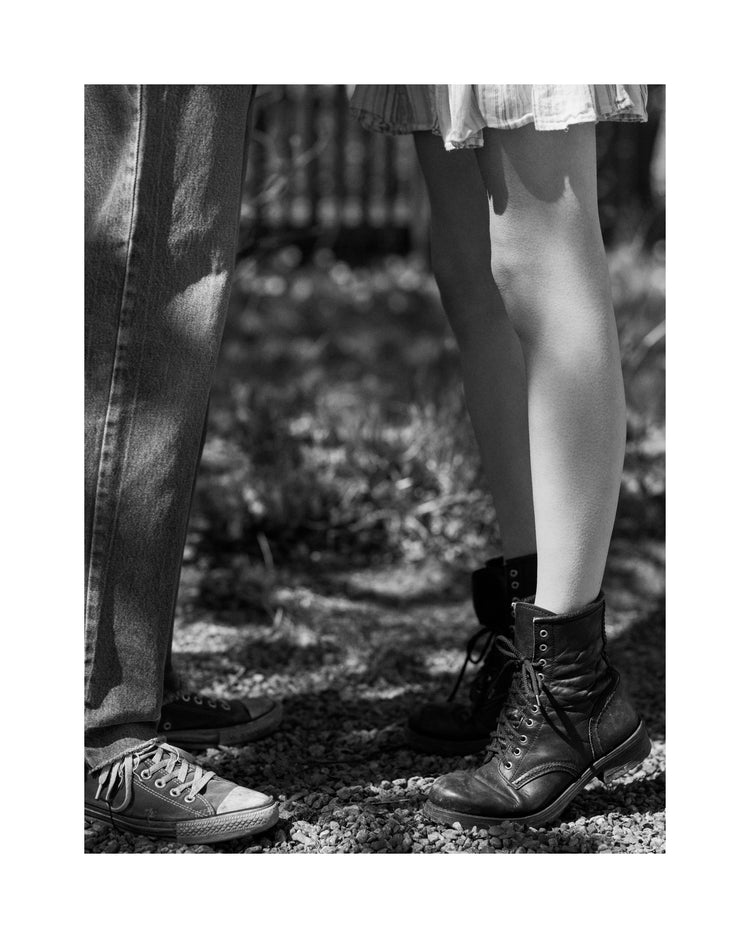 The feet of a woman standing on tiptoe kissing a man in converse sneakers.