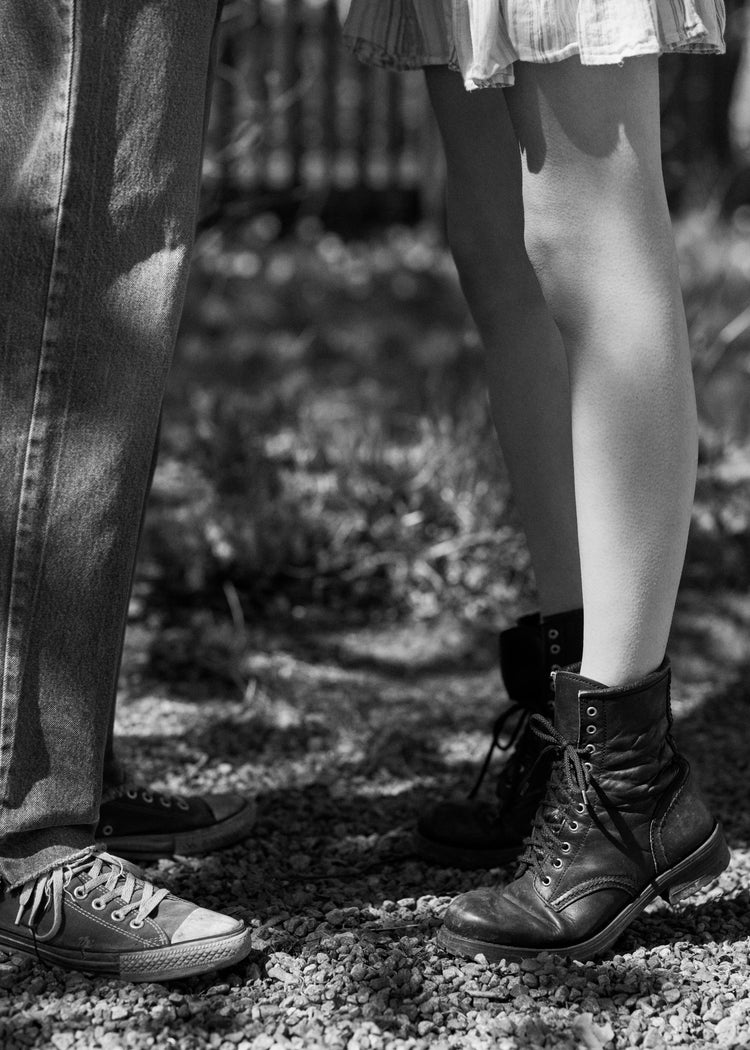 The feet of a woman standing on tiptoe kissing a man in converse sneakers.