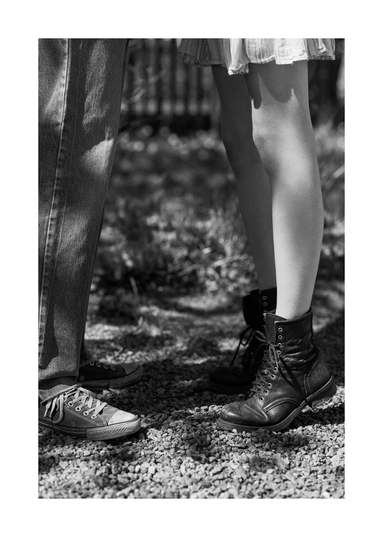 The feet of a woman standing on tiptoe kissing a man in converse sneakers.