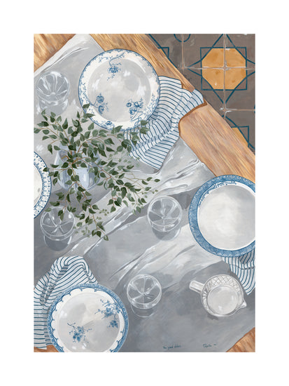 A meal setting featuring The Good Plates Poster, showcasing blue and white patterned plates, matching bowls, striped napkins, elegant glasses, and a white pitcher. A leafy plant adorns the center on a geometric tiled floor.