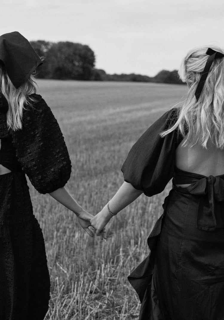 Two women dressed in black walking on a field and holding hands.