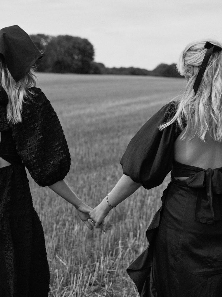 Two women dressed in black walking on a field and holding hands.