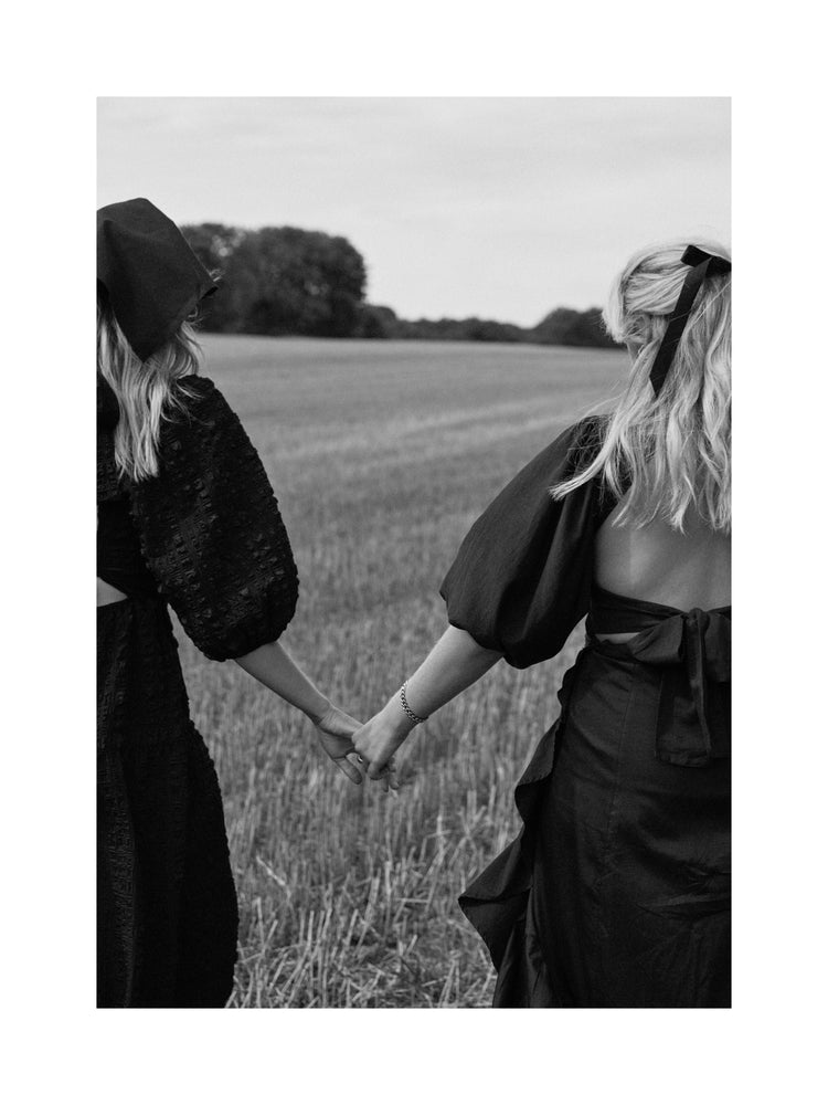 Two women dressed in black walking on a field and holding hands.