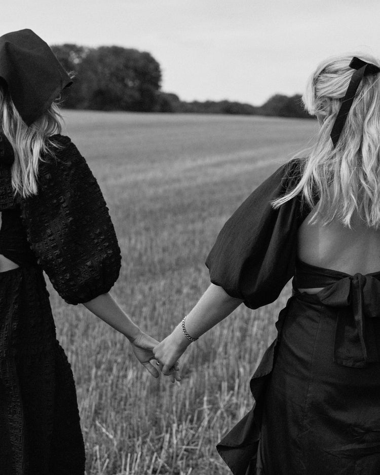 Two women dressed in black walking on a field and holding hands.