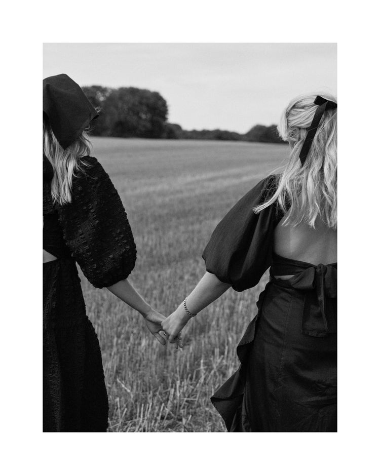 Two women dressed in black walking on a field and holding hands.