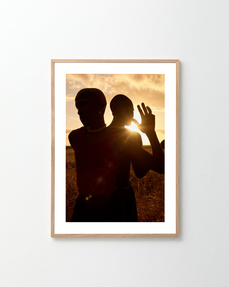 The Lets Play Like When We Were Young Poster beautifully portrays two silhouettes standing back-to-back, with one lifting a hand towards the sunset. Framed simply on a white wall, it captures the rustic charm of Bucks countryside at dusk.