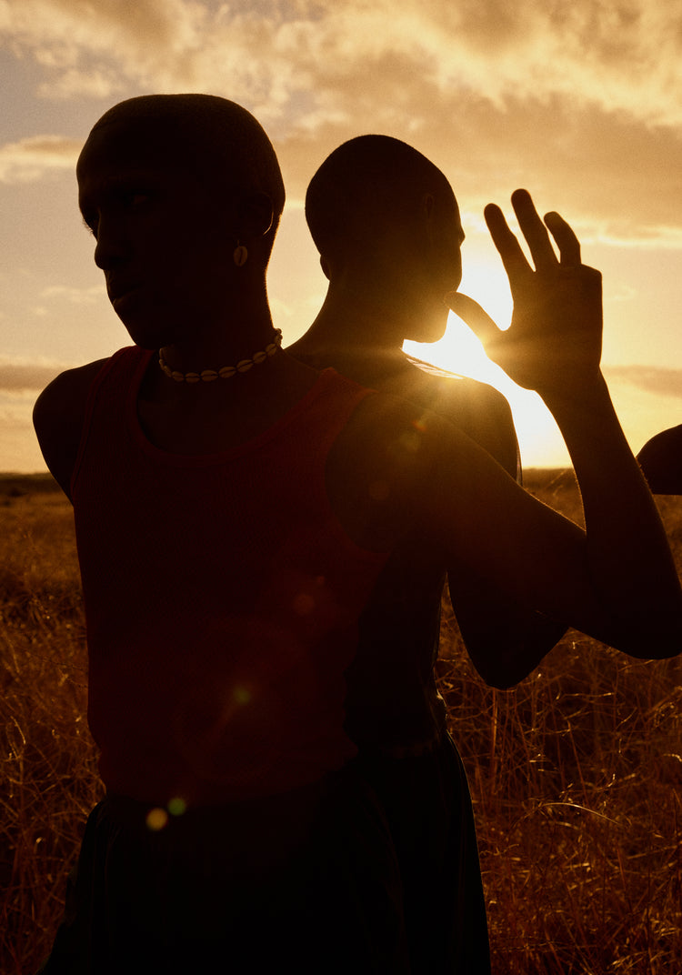 Two brothers standing back-to-back on an open field in the gazing sun.