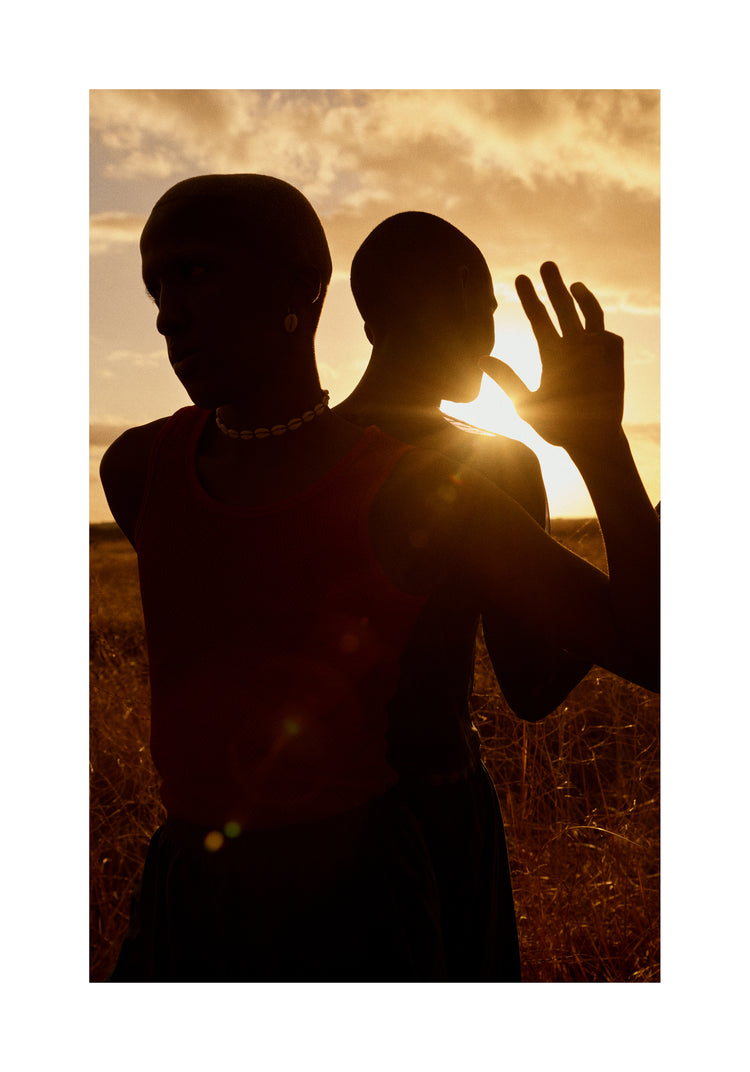 Two brothers standing back-to-back on an open field in the gazing sun.