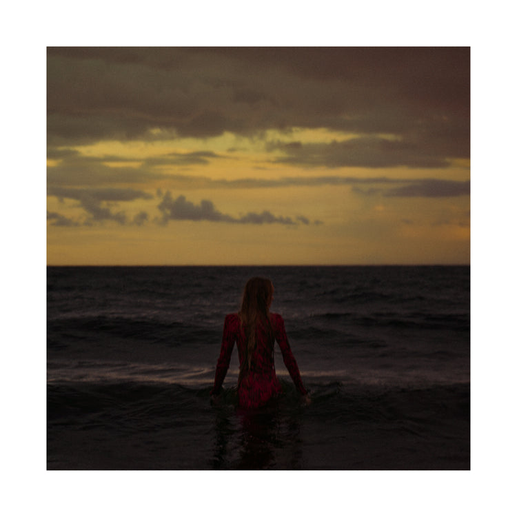 A woman in a red dressing gown walking into the ocean during sunset.