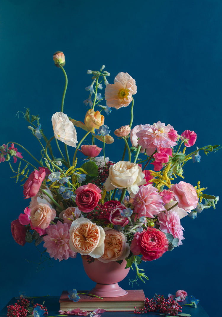 The Pink Kiss Poster showcases a vibrant bouquet of romantic flowers like roses and poppies in pink, white, and orange hues, set in a pink vase against a deep blue background. Elegantly styled with greenery and small red berries, it creates a lush, colorful display.