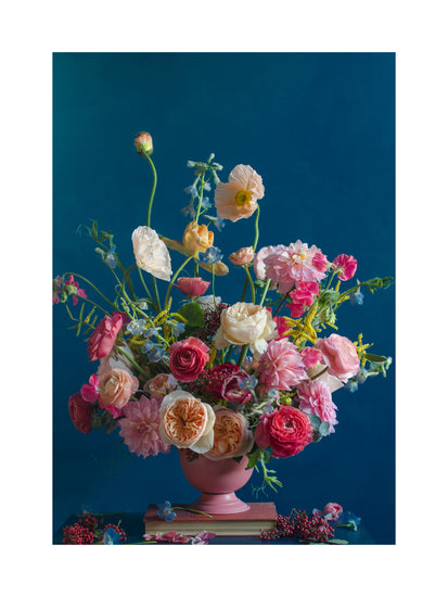 The Pink Kiss Poster showcases a vibrant floral arrangement in a pink vase on a blue background, featuring blossoms in pink, red, peach, and white with green foliage and berries. Its elegant style evokes classic romantic still life photography.
