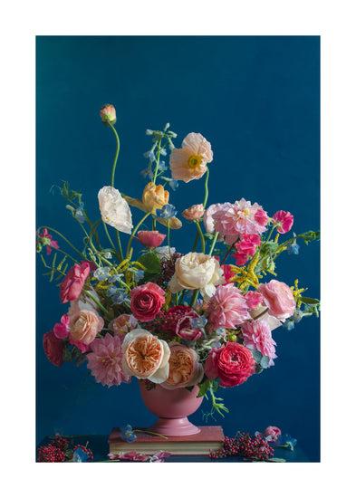 The Pink Kiss Poster showcases an elegant floral arrangement in a pink vase set against a deep blue background. It features roses, poppies, and wildflowers in pink, red, orange, and white hues with some blooms artfully scattered at the base, evoking romantic flowers.