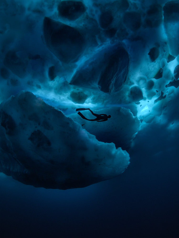 Diver swimming underneath ice bergs.