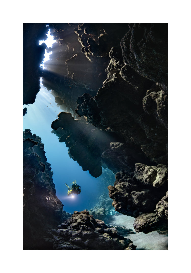 Diver swimming in the gap between cliff walls deep down in the ocean.