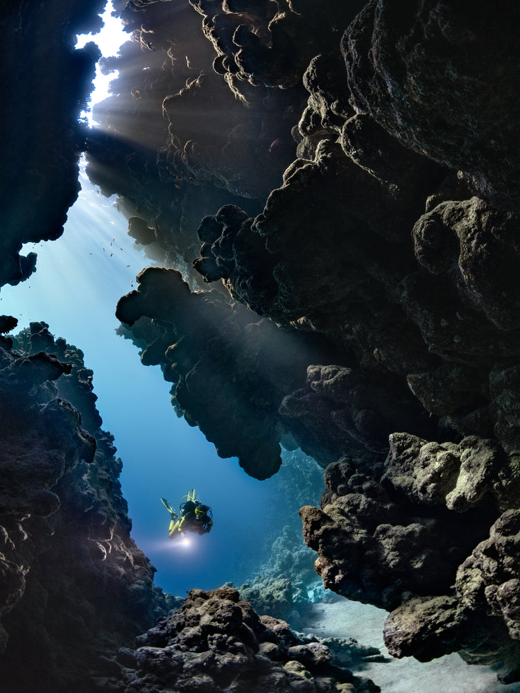Diver swimming in the gap between cliff walls deep down in the ocean.