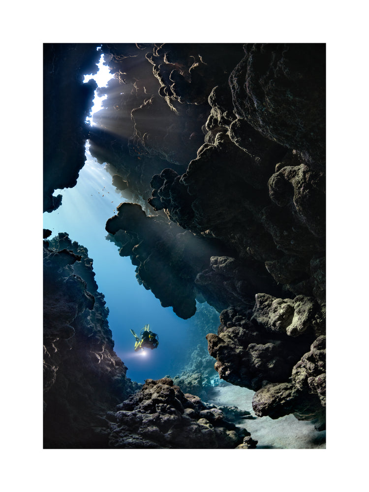 Diver swimming in the gap between cliff walls deep down in the ocean.