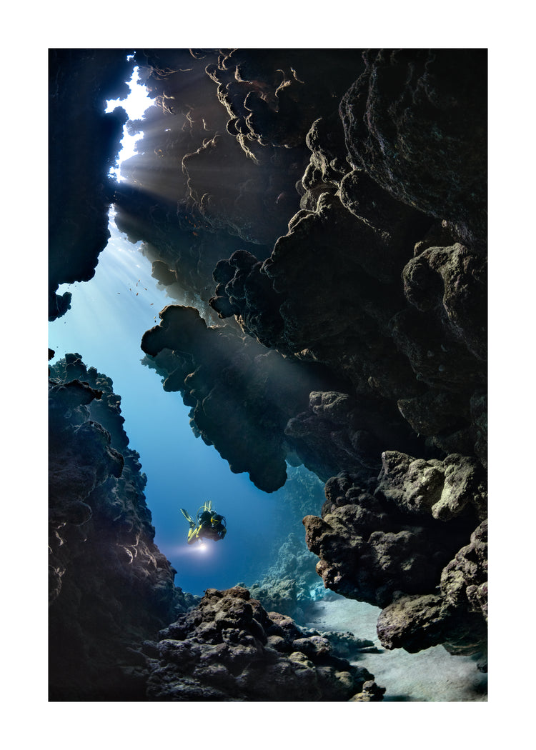 Diver swimming in the gap between cliff walls deep down in the ocean.