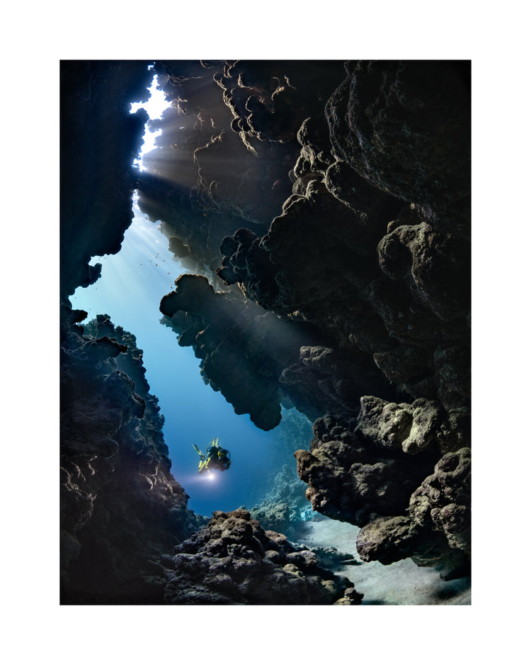 Diver swimming in the gap between cliff walls deep down in the ocean.