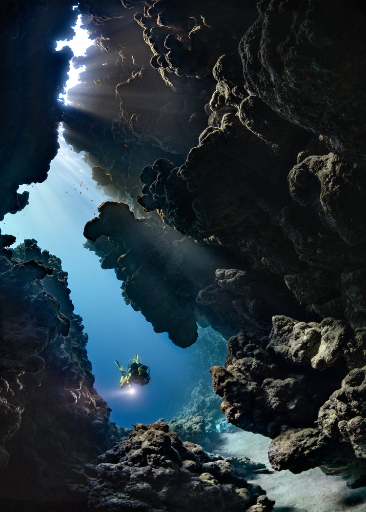 Diver swimming in the gap between cliff walls deep down in the ocean.