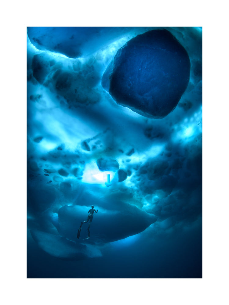 A diver swimming in the deep blue ocean underneath a surface made from ice.