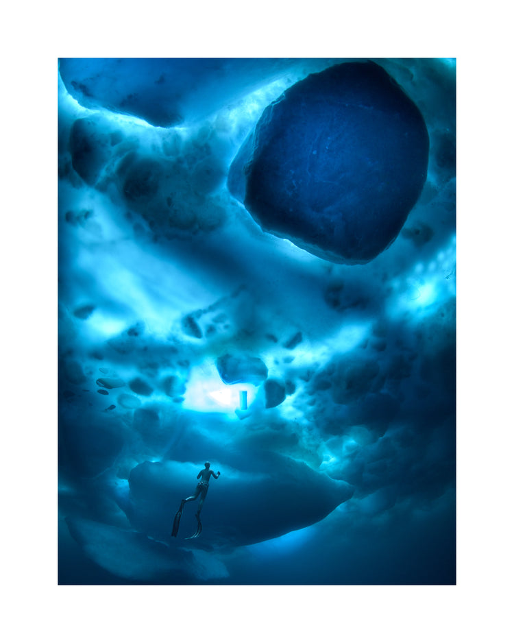 A diver swimming in the deep blue ocean underneath a surface made from ice.