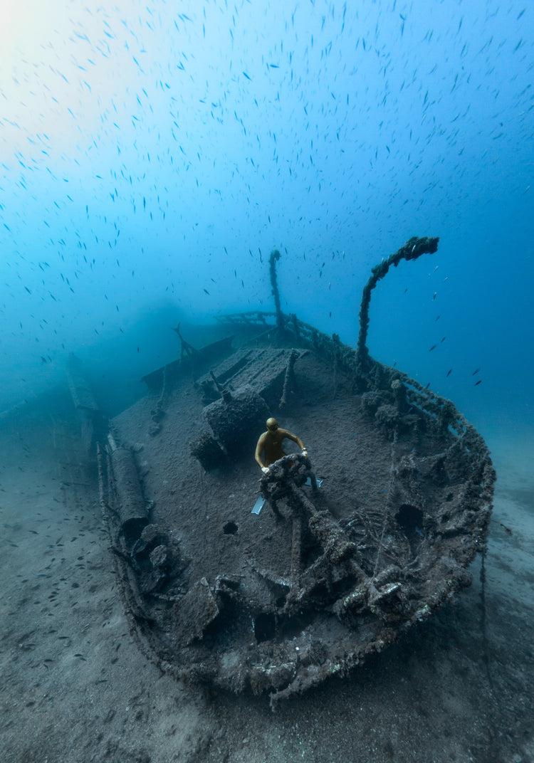 Shipwreck on the bottom of a deep blue ocean with a diver behind the wheel.