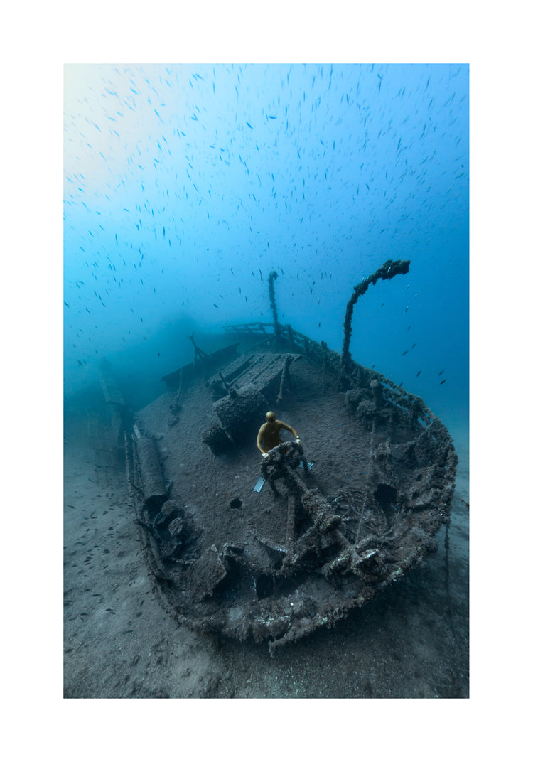 Shipwreck on the bottom of a deep blue ocean with a diver behind the wheel.