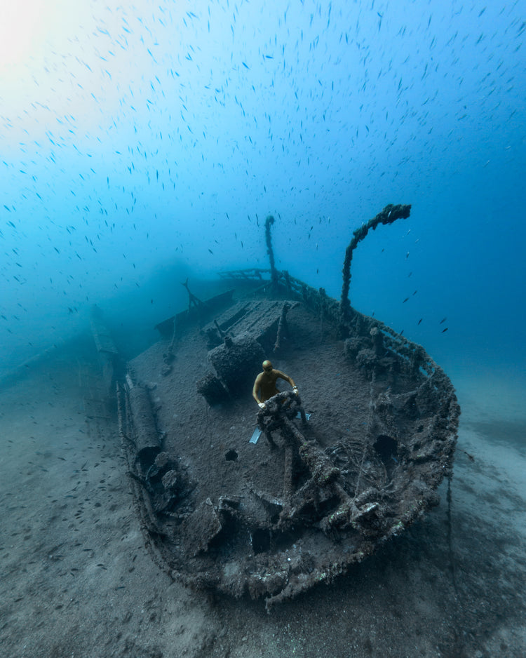 Shipwreck on the bottom of a deep blue ocean with a diver behind the wheel.