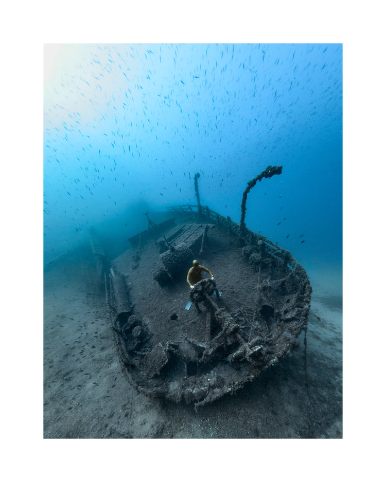 Shipwreck on the bottom of a deep blue ocean with a diver behind the wheel.